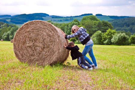 A girl and a boy pushing a round bundle of straw.
