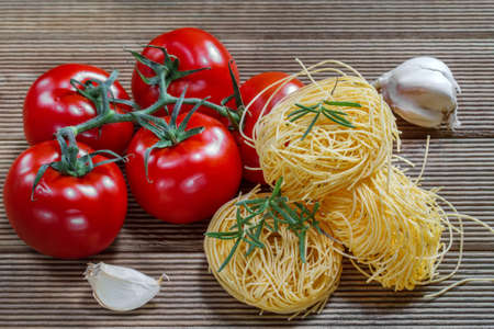 Pasta, tomatoes and herbs on a wooden tableの写真素材