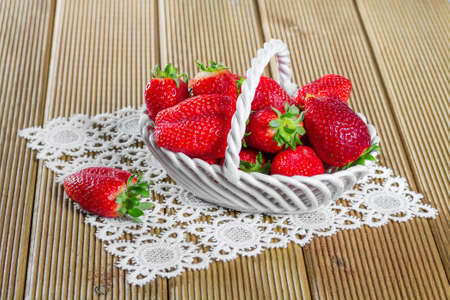 Ripe strawberries in ceramic basket on wooden backgroundの写真素材