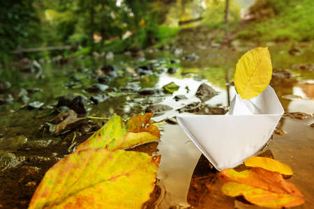 Change of seasons. Origami paper boat sailing from summer to autumnの写真素材