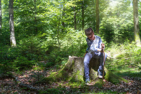 Young boy uses a knife to whittle a stick while out hiking in the forestの写真素材