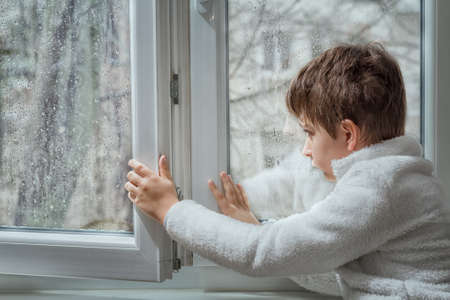 portrait of a pensive young man looking away through a wet window in a rainy day. Toned image.