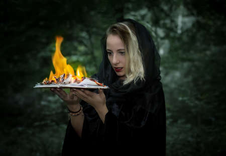 Young woman with a burning book in the forest. Haloween background.の写真素材