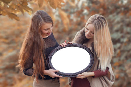 Two young women holding a photo frame. Place for text. Mock-upの写真素材