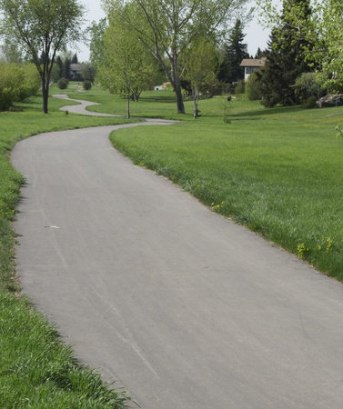 A windy paved park trail with trees, grass and the trail winding off in the distanceの写真素材