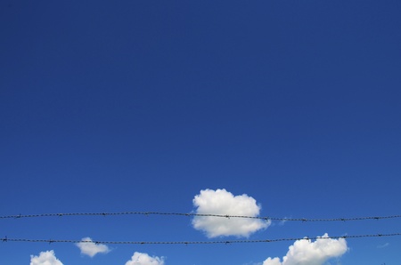 Light Blue sky with white clouds the bottom has two barbwire stretched across.の写真素材