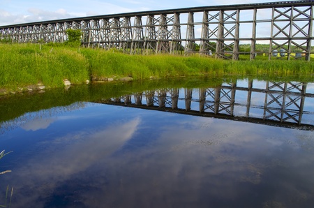 Old wooden train bridge  with a reflection in the water of the sky and bridge.の写真素材