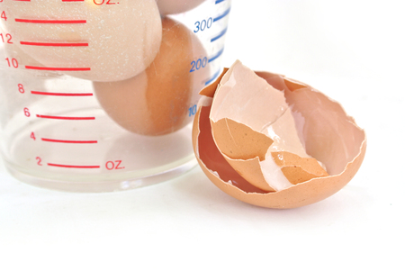 Broken egg closeup with egg in  measuring cup on white background
