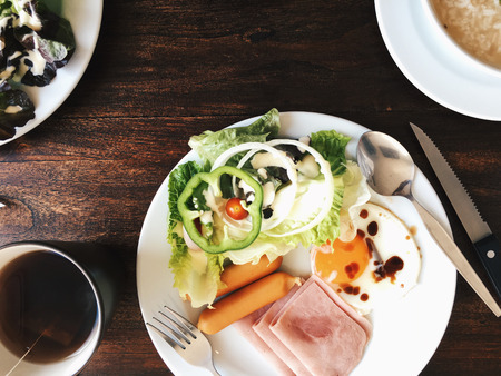 Overhead view of Hotel Breakfast - Soft boiled rice with fried eggs, bacon, sausages, ham, fresh salad, toast and hot tea on top a wooden tableの写真素材