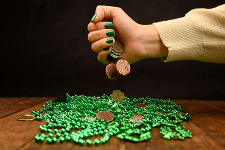 St. Patrick's concept. A woman's hand drops coins onto green clover necklaces.の写真素材