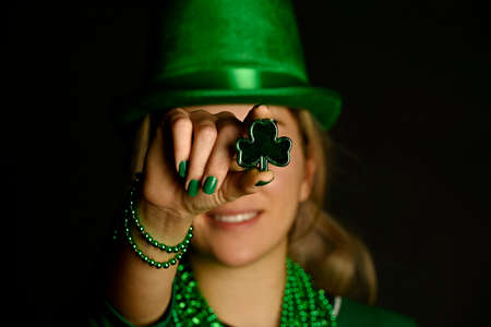 St. Patrick's concept. Girl in green hat shows her necklaces on black background.