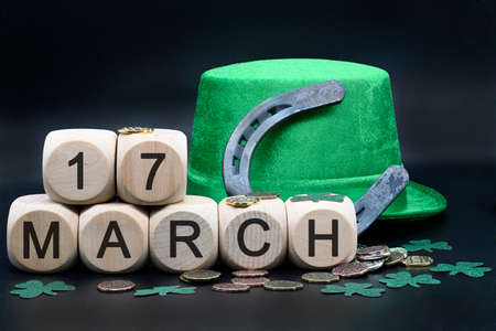 Concept of St. Patrick. Green hat, green necklaces and clovers, horseshoes, lucky coins and dice with letters March 17, St. Patrick's Day on black backgroundの写真素材