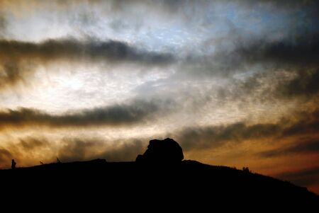 landscape with silhouette of a single rock in a hill at sunsetの写真素材