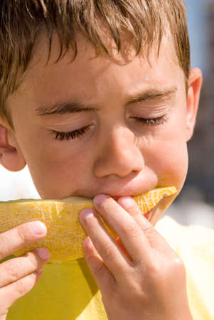 a six year old boy is eating melon on the beachの写真素材