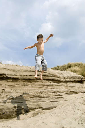a young boy jumping of the dunes into the sandの写真素材