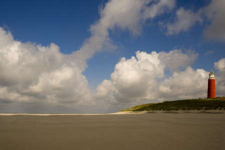 a lighthouse on the beach in Texel with a beautiful blue sky and clouds and lovely light on the sandの写真素材