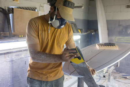 Surfboard making, woodworker wearing safety respirator sawing surfboard blank using handsawの写真素材