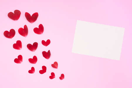 Pink background with rose petals in the shape of a heart, with rose, white candles and paper.の写真素材