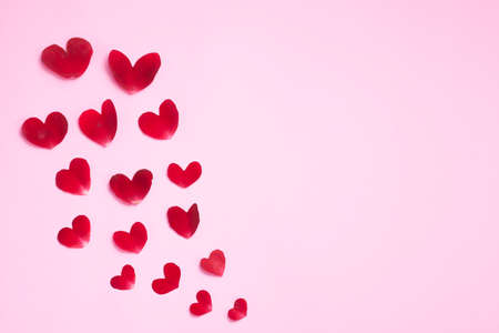 Pink background with rose petals in the shape of a heart, with rose, white candles and paper.の写真素材
