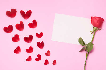 Pink background with rose petals in the shape of a heart, with rose, white candles and paper.の写真素材