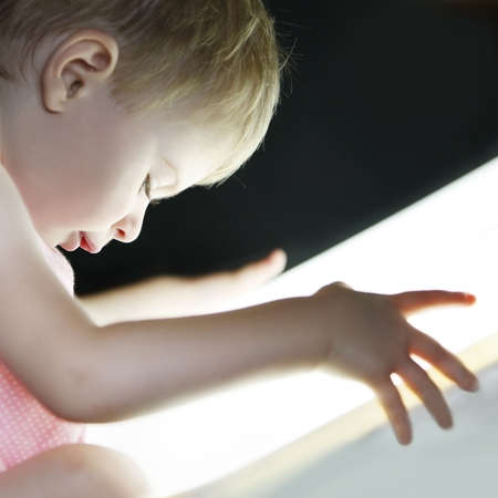 profile of a  girl looking very interested to a bright light close to her faceの写真素材