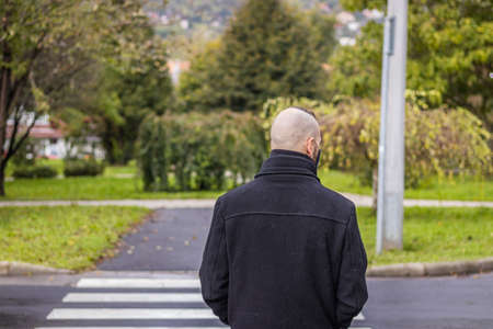 A man is standing in the dripping rain while wearing a mask at pedestrian crossing