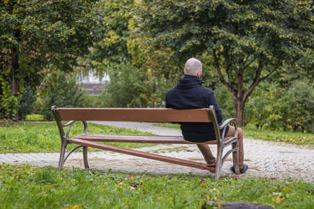 A man is sitting on a broken bench in the dripping rain in the local parkの写真素材