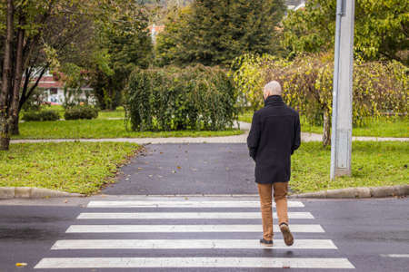 A man walks in the dripping rain while wearing a mask in a small city in Hungaryの写真素材