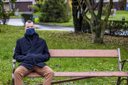 A man is sitting on a broken bench in the dripping rain in the local parkの写真素材