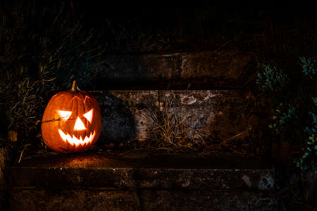 Spooky Halloween pumpkin lantern on concrete stairs in the garden at nightの写真素材