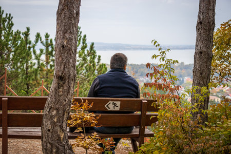 A man sits on a bench at the light cross look out at the top of the Csandor mountain in Vonyarcvashegy, Hungaryの写真素材