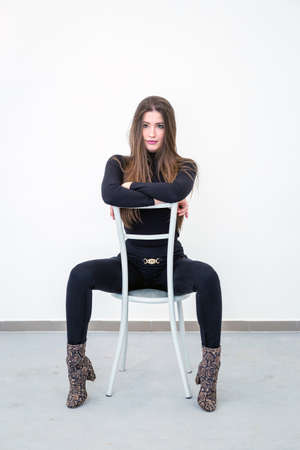 Beautiful young woman sitting on a chair over white wallの写真素材