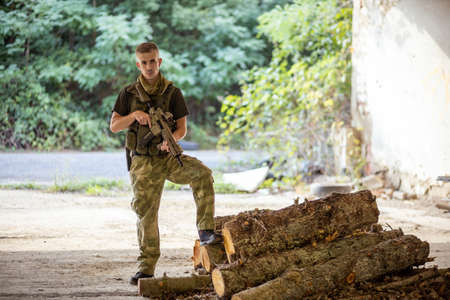 A man standing with an airsoft assault rifle in military uniform in concrete hangarの写真素材