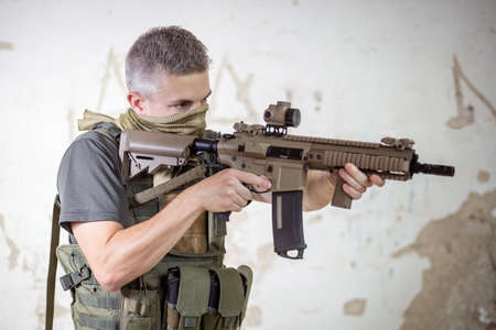 A man standing with an airsoft assault rifle in military uniform in concrete hangar