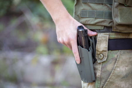 Close up of a man holding an airsoft pistol in military uniform