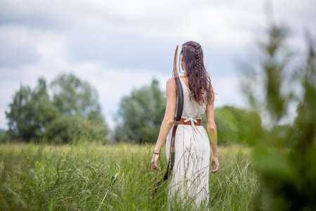 A Hungarian woman in a linen dress standing with a bow in the tall grassの写真素材