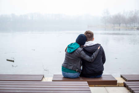 Young couple sitting at Lake Gebart (Zalaegerszeg, Hungary) on a foggy winter dayの写真素材