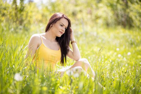 Young woman in yellow top sitting on grass in summerの写真素材