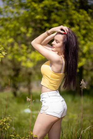 Young woman in yellow top and white shorts standing in nature in summerの写真素材