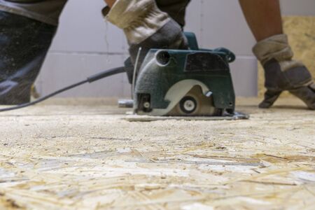 Close-up manual circular power saw in the hands of a worker in a home workshop.の写真素材