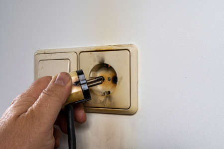 Hand Removing Plug From An Over Heated Socket