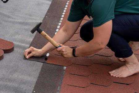 Woman laid of bitumen roof shingles. Disregard of occupational health and safety.の写真素材