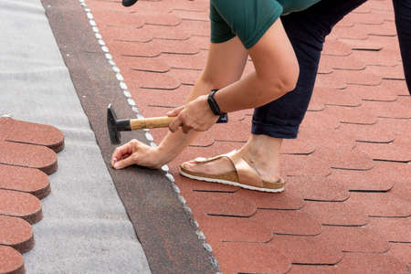 Woman laid of bitumen roof shingles. Disregard of occupational health and safety.の写真素材