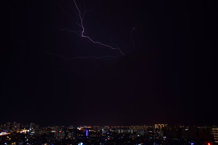 The city skyline is illuminated by a bright lightning bolt that streaks across the dark sky. The...
