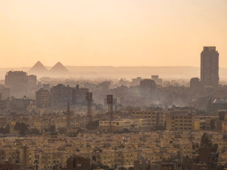 A city with a large building in the background. The sky is a light orange color. There are two pyramids in the distanceの写真素材