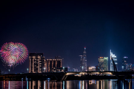 A city skyline with a bridge in the middle. The bridge is lit up with lights. There are fireworks in the skyの写真素材