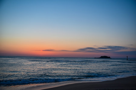 The ocean is calm and the sky is a beautiful shade of blue. The sun is setting and the sky is filled with a warm orange glowの写真素材