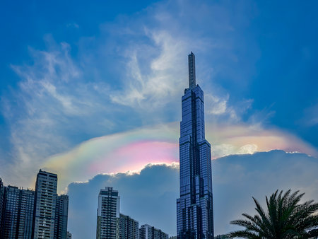 A tall building with a rainbow on top. The rainbow is in the sky. The building is in the city
