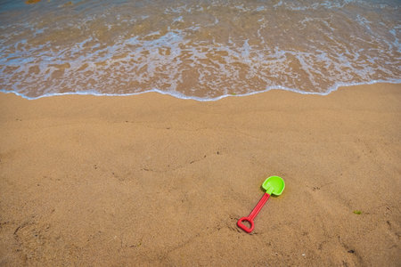 A green plastic shovel is laying on the sand. The shovel is on the beach near the waterの写真素材