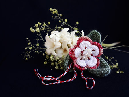 Handmade crocheted flower, with red and white string, known as Martisor. It is a Romanian traditional symbol of the beginning of spring. Isolated on black background.の写真素材